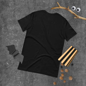 Black unisex t-shirt back view on textured surface with wooden sticks, decorative bat, and googly eyes.