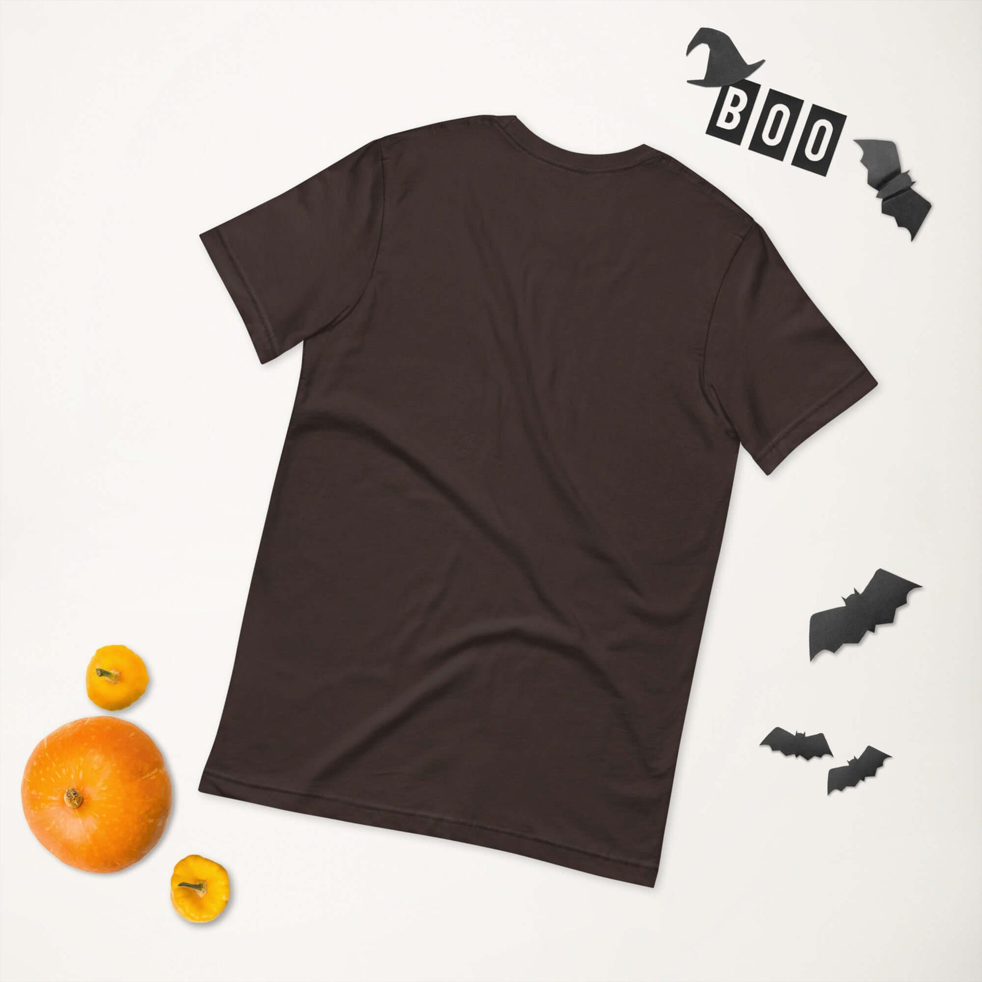 Back view of a black unisex t-shirt with Halloween decorations including pumpkins and bats nearby.