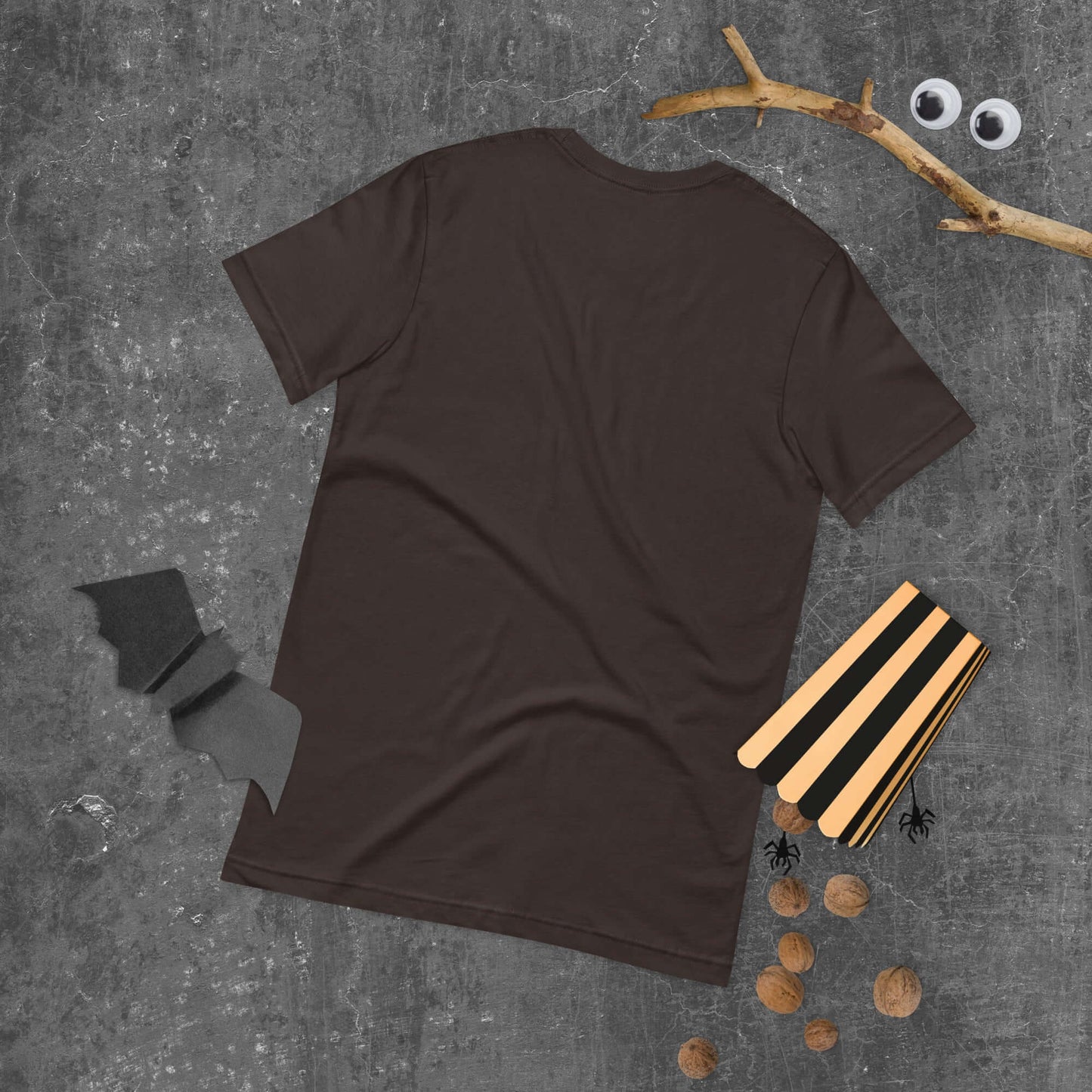 Unisex dark brown t-shirt laid flat with halloween decorations on a textured surface