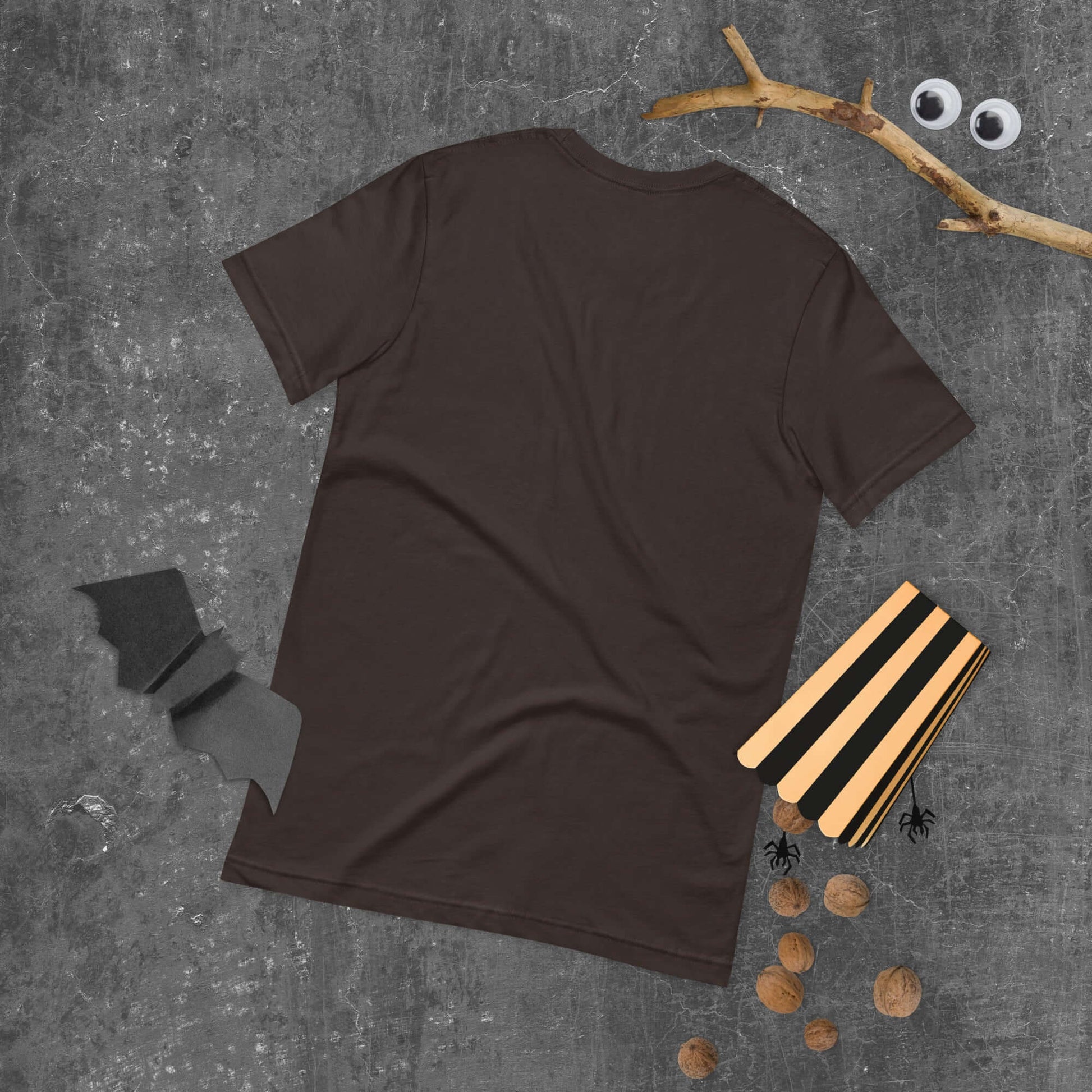 Unisex dark brown t-shirt laid flat with halloween decorations on a textured surface