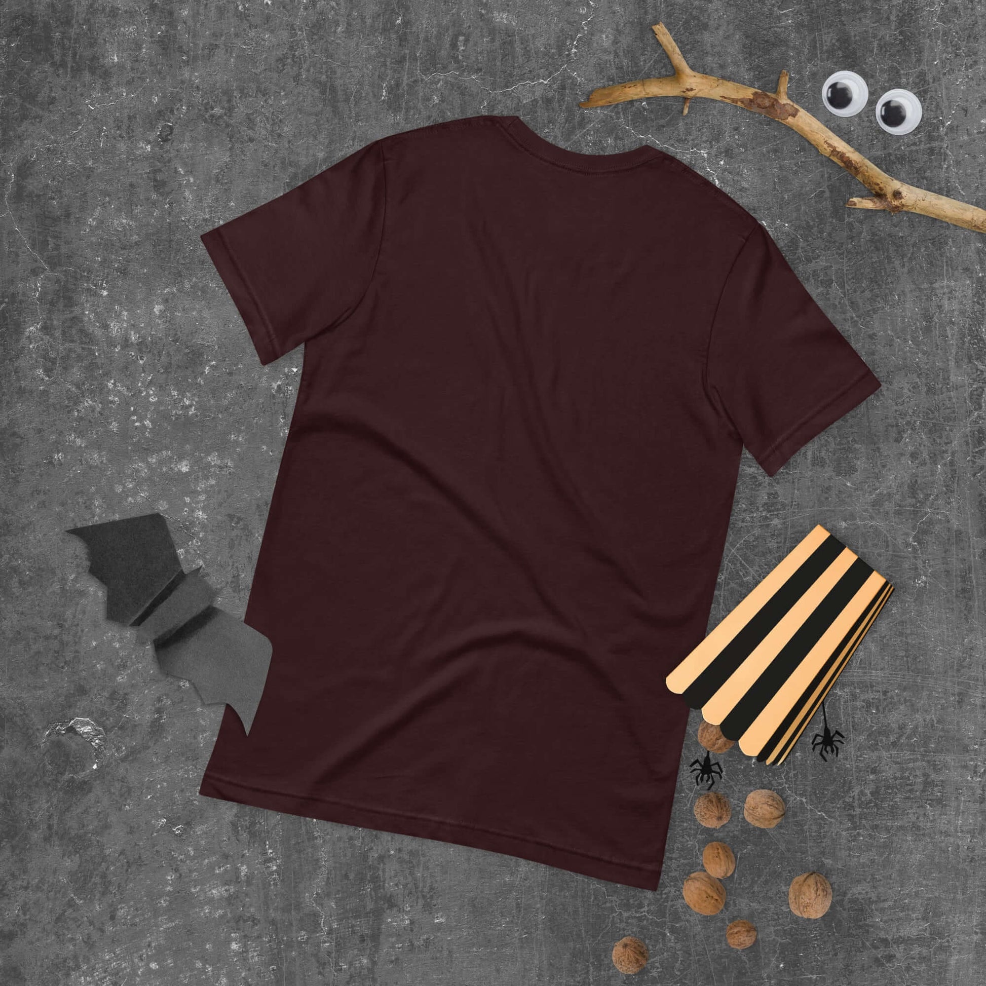 Maroon unisex t-shirt on a gray textured background with Halloween props